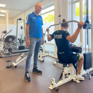 Patiënt voert een lat pulldown uit onder begeleiding van een fysiotherapeut