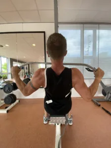 Patiënt traint de kracht van schouders en bovenrug onder begeleiding van een fysiotherapeut.