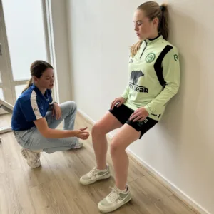 Fysiotherapeut begeleidt een vrouwelijke sporter tijdens een knieoefening